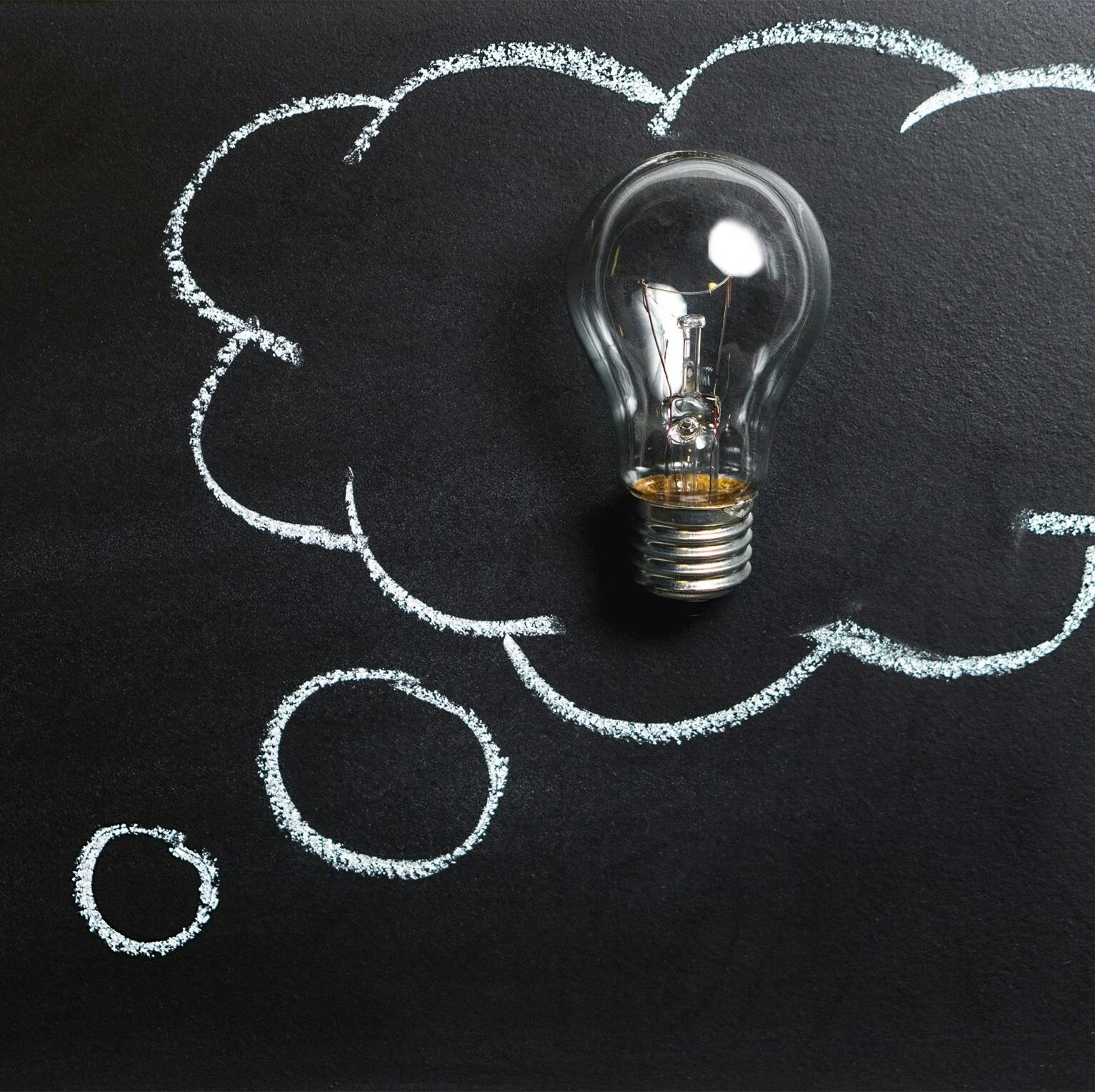 Light bulb laying on chalkboard with drawn thought bubble, symbolizing creative ideas.